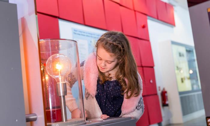 a young girl presses buttons in front of a large light bulb to make it glow.